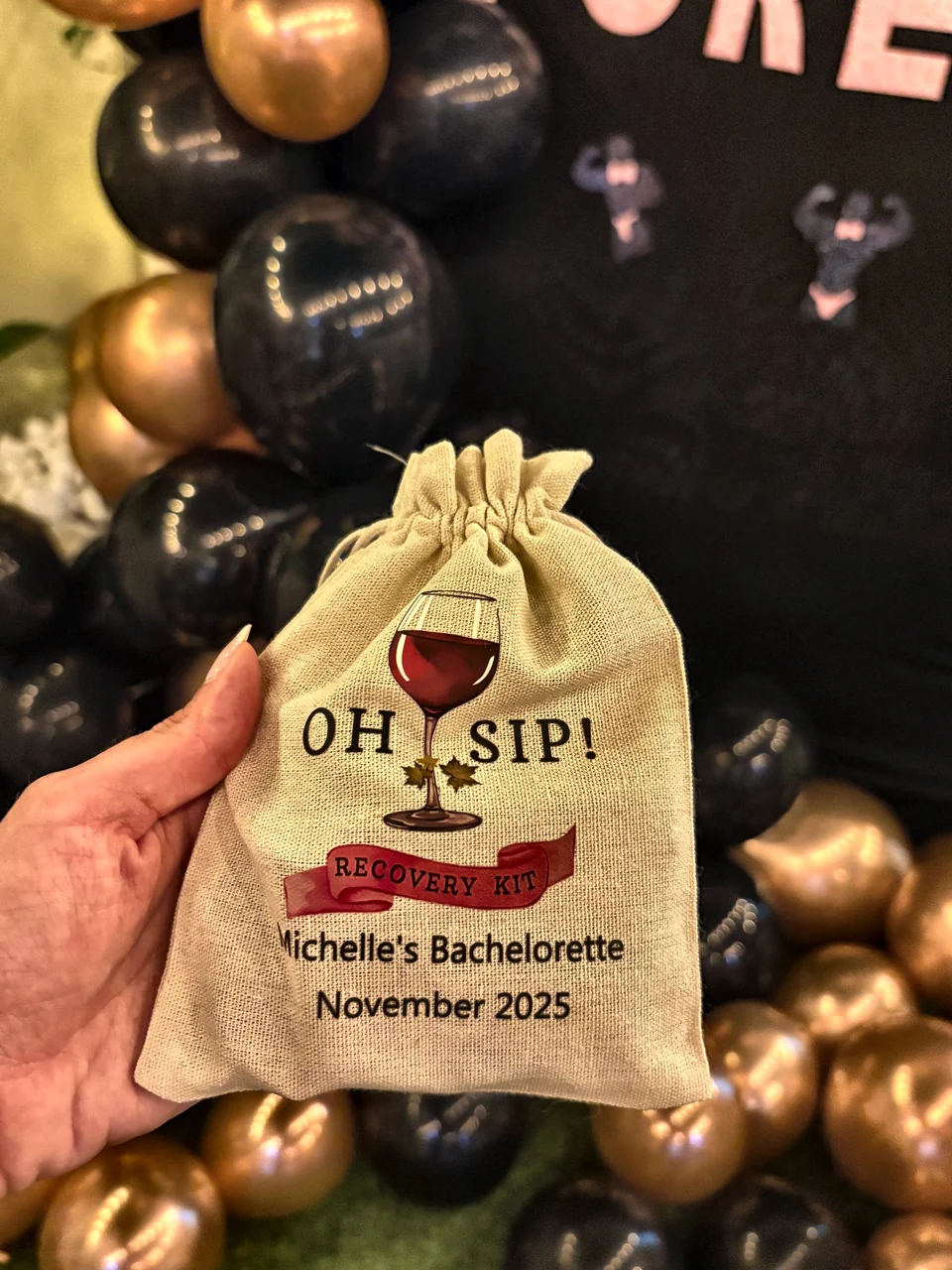 Personalised Oh Sip recovery kit bag held up against black and gold balloons